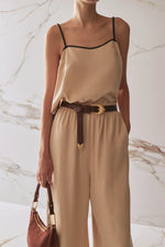 Woman wearing a beige top and pants with a brown belt against a marble background