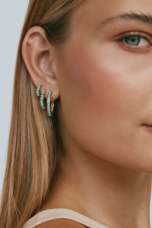 Close-up of a woman wearing turquoise hoop earrings against a neutral background