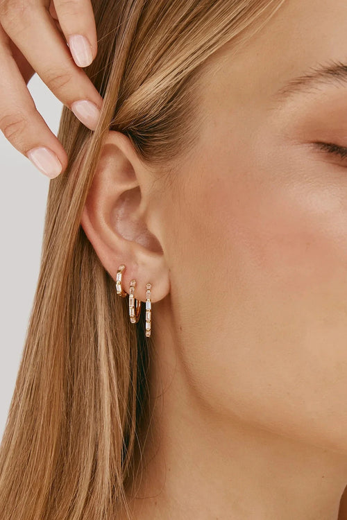Close-up of a woman wearing gold hoop earrings with a neutral background