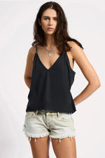 Woman wearing a black tank top and light denim shorts on a white background