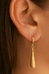 Gold teardrop earring worn by a person with dark hair.