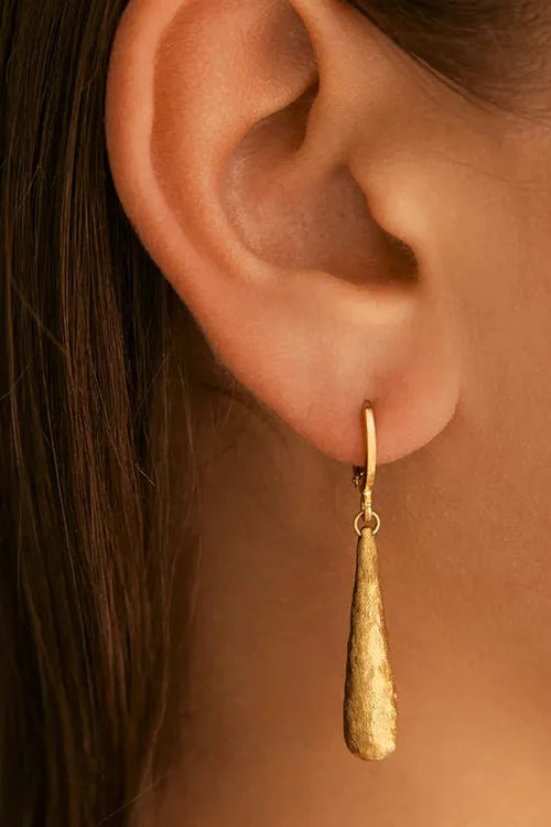 Gold teardrop earring worn by a person with dark hair.
